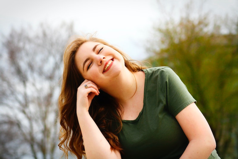 A woman is smiling outside. She has long red hair and is wearing a green t-shirt. There are trees in the background. Find out more about self-compassion today in our blog! Contact us to book your first counselling session!