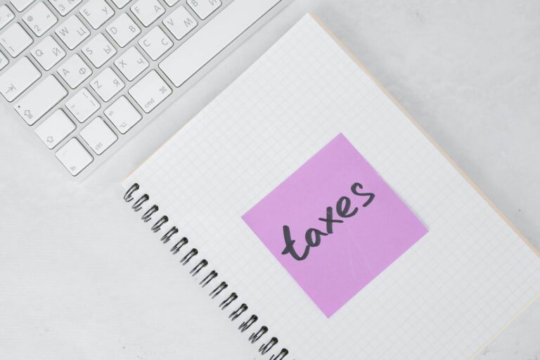 White keyboard and a white note pad lay on a white desk. The note pad has a purple sticky note with the word "taxes' written on it. Contact trauma informed, EMDR and Somatic Experiencing trained therapists today. Mental health support available online across Ontario.